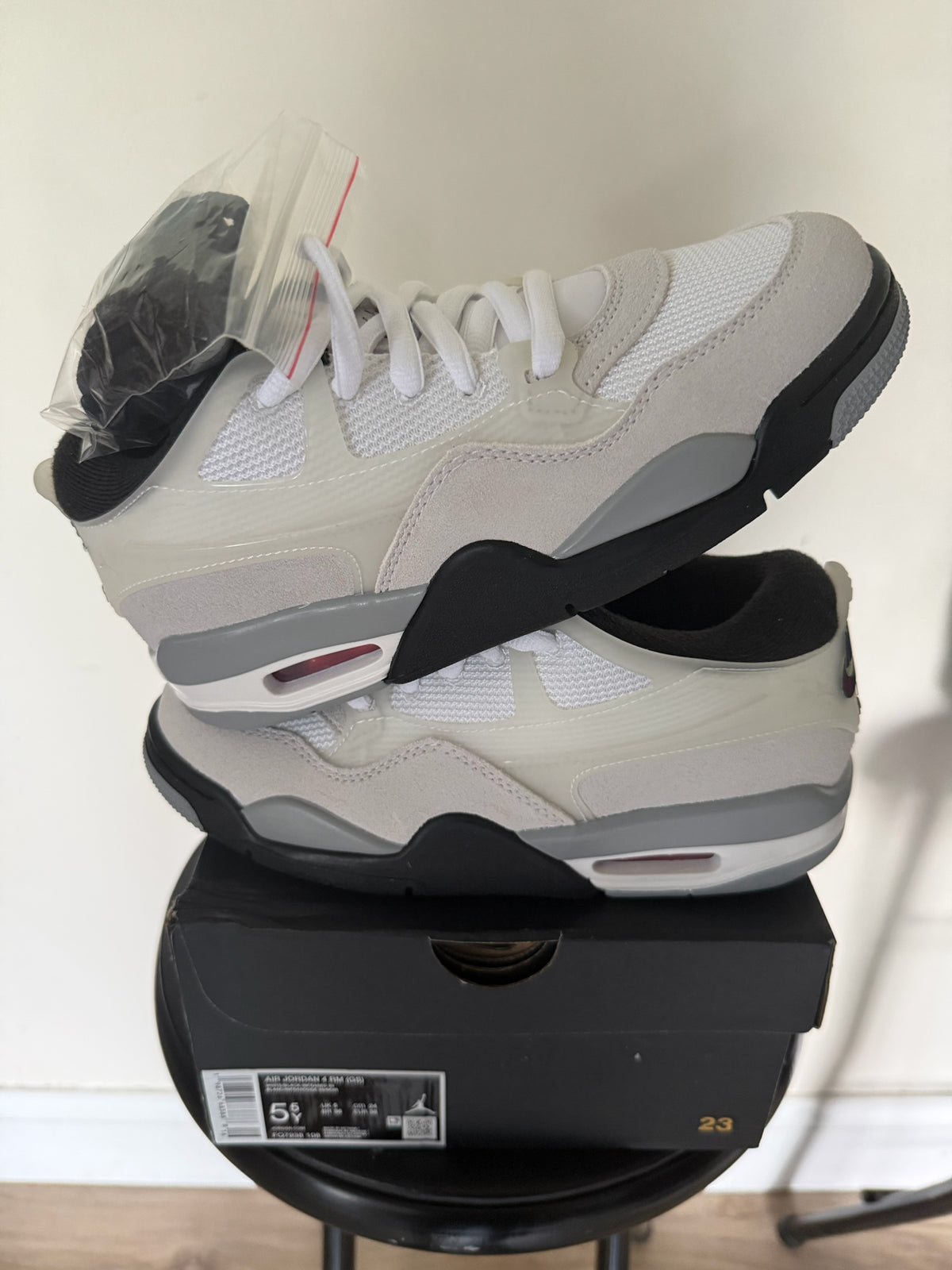 D’s Laces Jordan 4 RM sneakers in light bone, grey, and white mesh and suede stacked on a black shoebox
